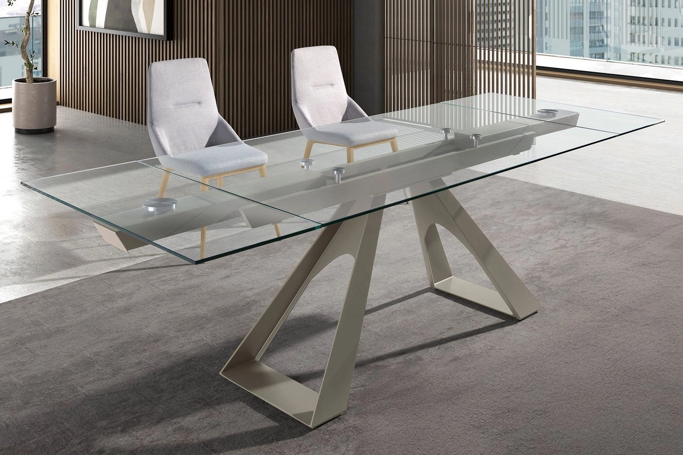 Mesa com tampo de vidro extensível e base metálica angular, duas cadeiras cinzentas.