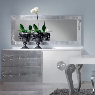 Aparador prateado com espelho retangular ornamentado e vasos prateados com orquídea