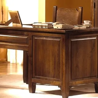 Secretaria de madeira escura com cadeira, candeeiro, livros e chávena.