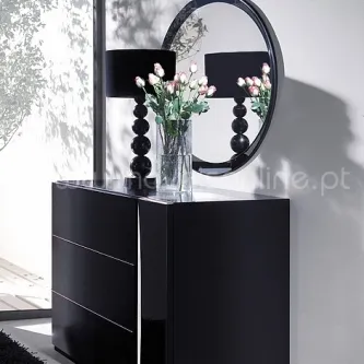 Cómoda com moldura circular, acabamento preto, abajur e vaso com ramos florais.