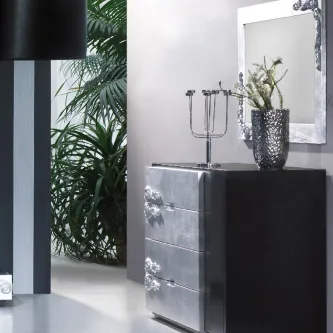 Cómoda preta com moldura prateada, puxadores ornamentados e vaso decorativo