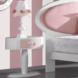 Mesa de cabeceira branca e rosa com gaveta com laço, abajur com flores e cabeceira oval rosa