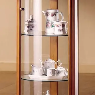 Vitrine redonda com prateleiras de vidro exibindo serviço de chá em porcelana