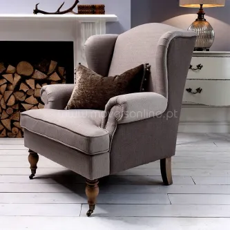 Poltrona Helena cinza de pernas em madeira, almofada castanha, junto a lareira