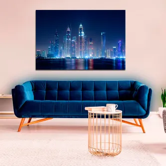 Quadro Dubai com skyline noturno de arranha-céus refletidos na água, pendurado acima de sofá azul