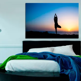 Quadro com silhueta a meditar junto ao mar ao pôr do sol, pendurado sobre a cama