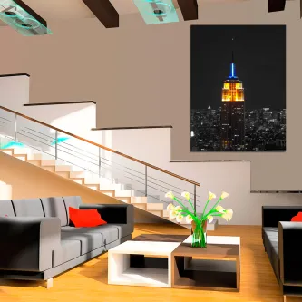 Quadro Empire State iluminado à noite, topo azul e laranja numa sala moderna