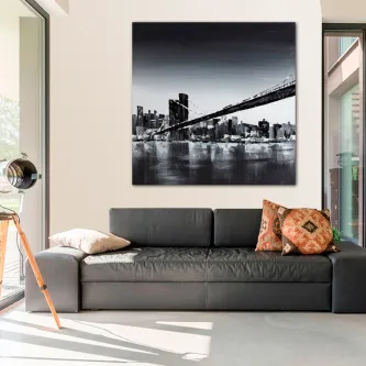 Quadro a preto e branco da ponte de Nova Iorque sobre o rio, exibido acima de sofá cinzento.