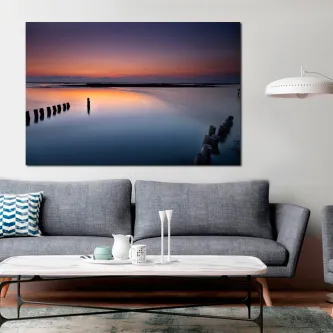 Quadro Amanhecer Marítimo com mar calmo, céu alaranjado e estacas de cais