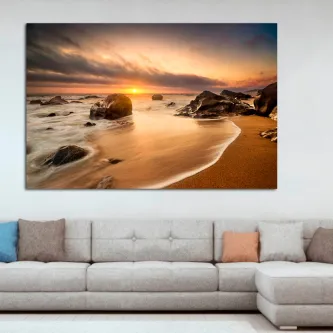 Quadro de praia rochosa ao pôr do sol sobre sofá cinzento
