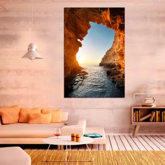 Quadro de gruta rochosa com vista para o mar ao pôr do sol, exposto numa sala moderna
