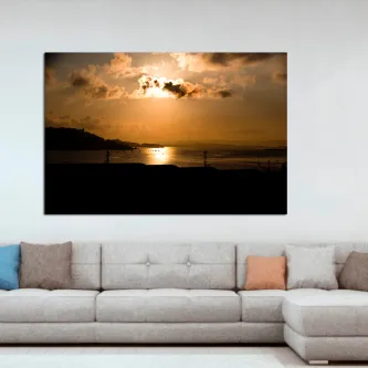 Anoitecer na praia com sol por trás das nuvens e reflexo na água.