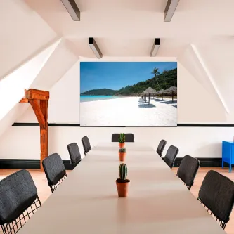 Sala de reunião com quadro marinho paradisíaco na parede e mesa longa com vasos