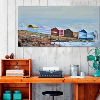 Quadro com casinhas de praia coloridas junto à água, pendurado sobre secretária de madeira.