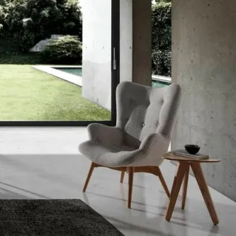 Poltrona Duo cinzenta com estofado felpudo e pernas de madeira junto a mesa lateral