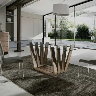 Mesa de jantar Ete com tampo de vidro e base em madeira geométrica, ambiente luminoso.