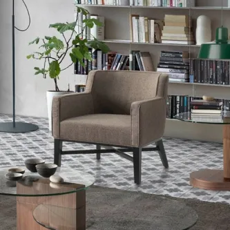 Poltrona Alfa estofada castanho-acinzentada com pernas de madeira em sala com estante