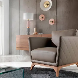 Poltrona Luna cinzenta estofada com pés em madeira, junto a móvel e candeeiro