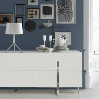 Aparador inox branco com pernas metálicas, lâmpada, loiça e quadros numa parede azul