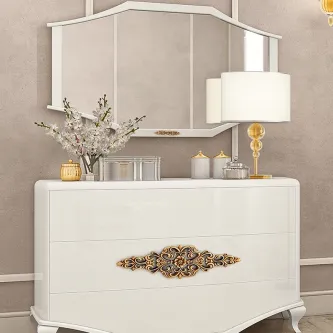 Comoda branca com espelho, ornamento dourado central, candeeiro e vaso de flores