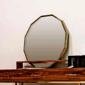 Espelho alfaiate com moldura dourada facetada apoiado numa cómoda de madeira