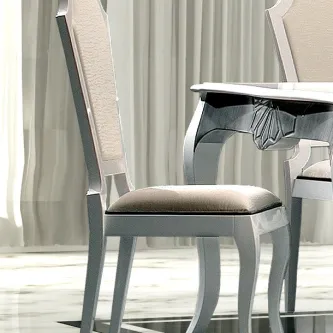 Cadeira Splendid estofada bege com costas altas e pernas prateadas junto a mesa