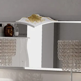Espelho Khyara com moldura branca e ornamento dourado no topo, reflexo de candeeiros e vaso