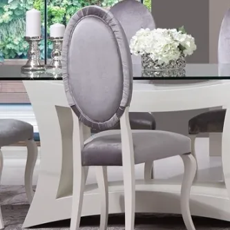 Cadeira com encosto oval estofado prateado e pernas brancas junto a mesa de jantar