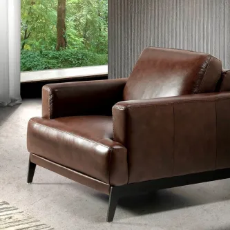 Cadeirão castanho em pele com pés metálicos e estofos acolchoados junto à janela