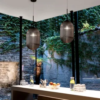 Dois candeeiros de teto Athena Oval pendentes sobre balcão com parede de pedra e vegetação