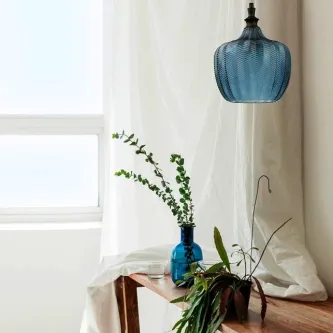 Candeeiro de teto Loni azul em vidro pendente sobre mesa com plantas