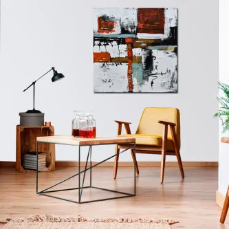 Quadro abstrata colorido pendurado em parede branca acima de poltrona amarela e mesa de centro.