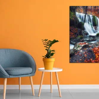 Sala com parede laranja, poltrona azul, planta e quadro de cachoeira em floresta