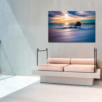 Pintura de pôr do sol sobre o mar com rocha, pendurada acima de sofá claro