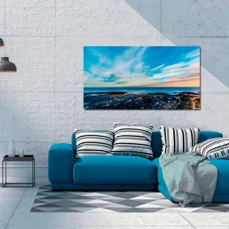 Pintura de mar calmo com rochas e céu colorido sobre sofá azul