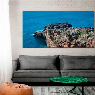 Imensa pintura marítima com falésia rochosa e mar azul pendurada acima de sofá