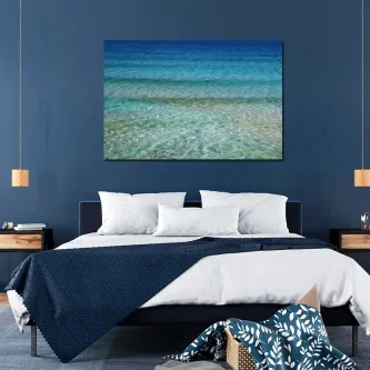 Pintura de águas cristalinas em tons de azul pendurada acima de cama moderna.