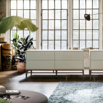 Aparador Verona branco de três gavetas em sala com grandes janelas e plantas