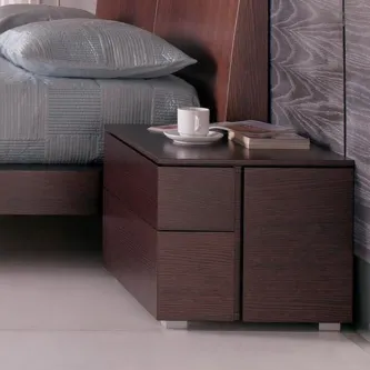 Mesa de cabeceira Visio em madeira escura com três gavetas ao lado da cama