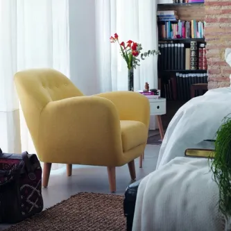 Cadeirão Gerunda amarelo junto à cama com mesa de cabeceira e estante