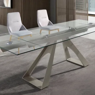 Mesa com tampo de vidro extensível e base metálica angular, duas cadeiras cinzentas.