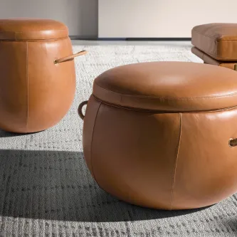 Pufes Luter redondo em pele castanha com alça, sobre tapete cinzento
