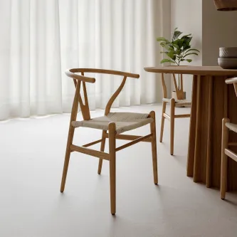 Cadeirão Ada em madeira clara com assento trançado, ao lado de mesa de jantar