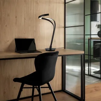 Candeeiro de mesa Danza preto curvo iluminado sobre secretária de madeira