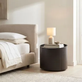 Mesa de cabeceira Iza redonda preta com candeeiro e livros ao lado da cama