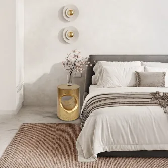 Mesa de apoio Hole dourada com abertura circular ao lado de cama minimalista