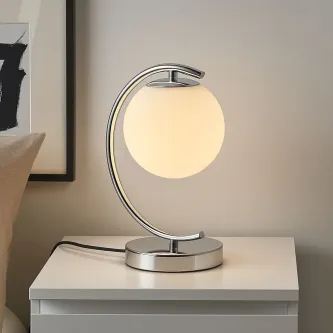 Candeeiro de mesa com bola de vidro e estrutura metálica curva sobre cómoda branca