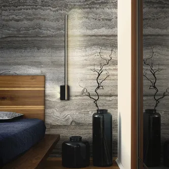 Aplique stick vertical minimalista em parede de pedra junto à cama e vasos negros