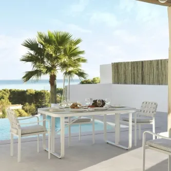 Mesa de jardim Kurve branca com quatro cadeiras em terraço junto à piscina e vista para o mar