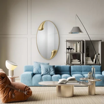 Espelho oval Daisy com apontamentos dourados sobre sofá azul em sala moderna